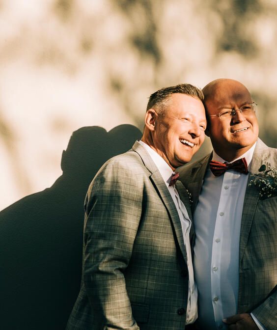 Happy well-dressed gay men standing against wall during wedding